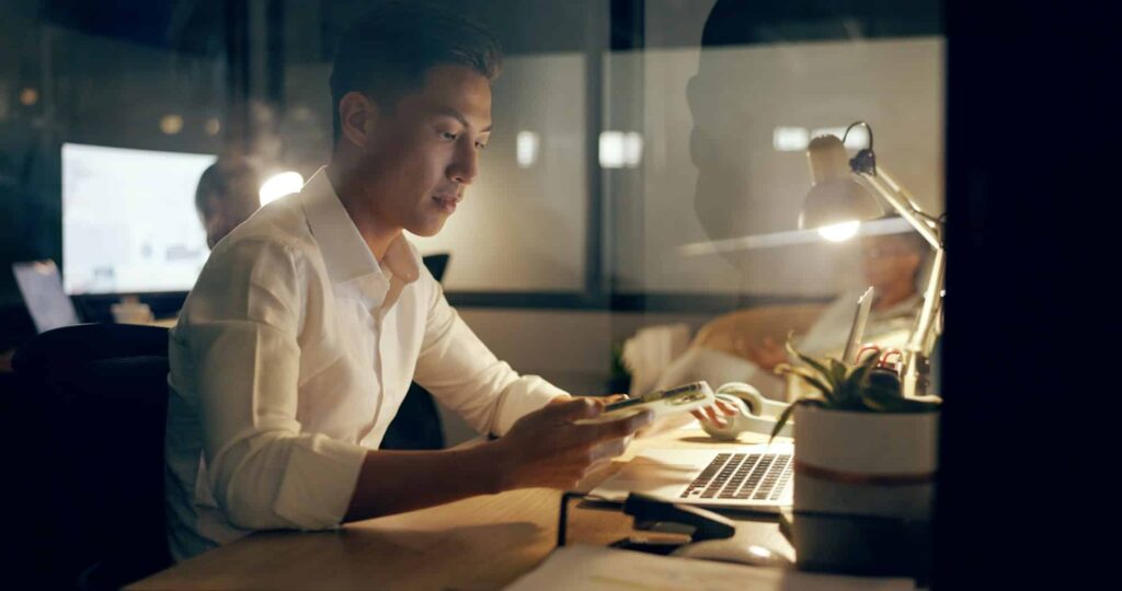 Asiatischer Geschäftsmann, Laptop und Telefon, der nachts im Büro im Bereich Marketing oder Werbung arbeitet. Japaner