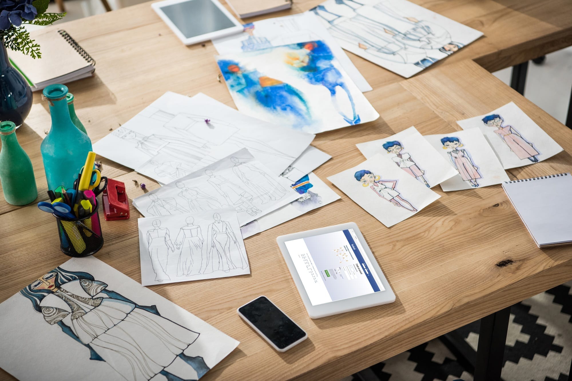 un smartphone, une tablette numérique avec le site Facebook et des croquis de mode posés sur la table