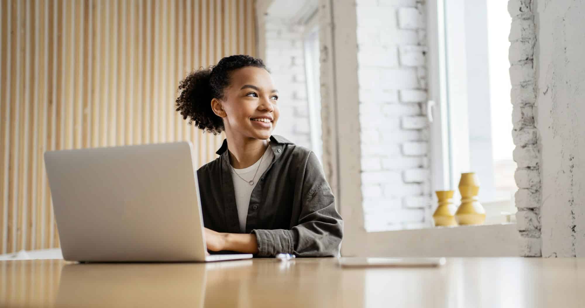 Jeune femme souriante travaillant sur son ordinateur portable dans un loft moderne, incarnant la productivité