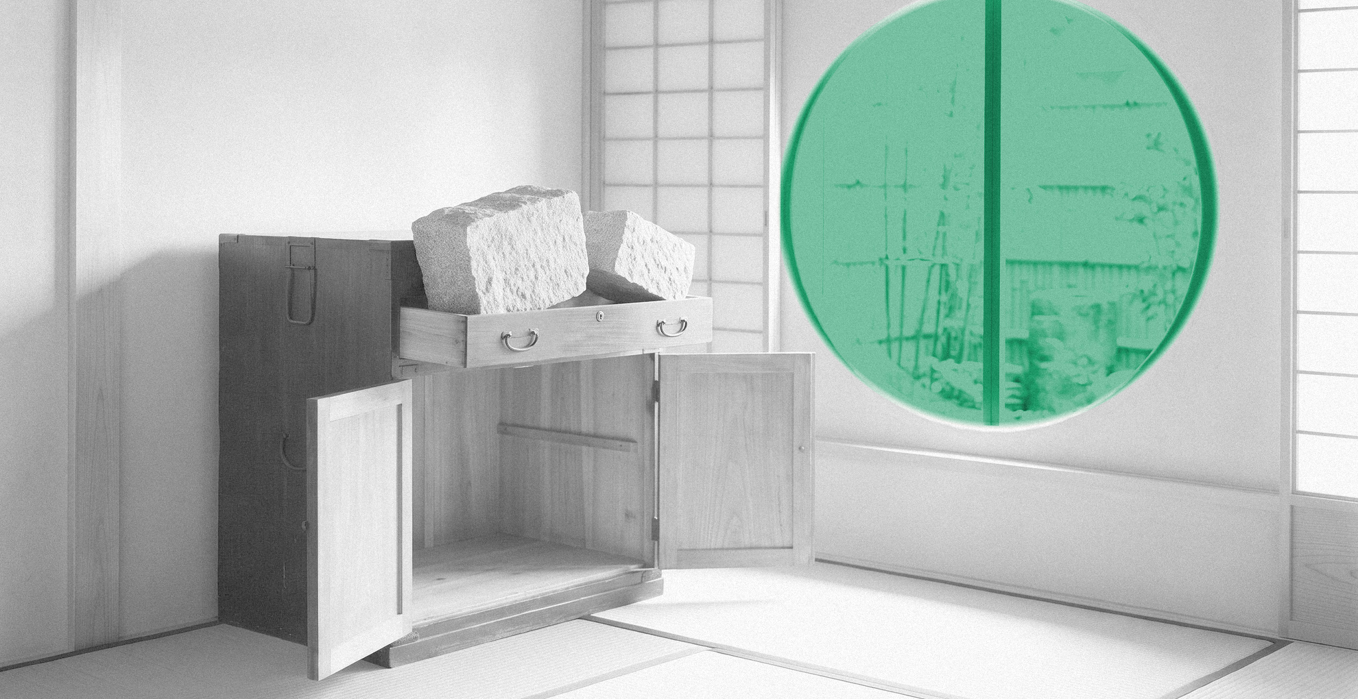 Black-and-white Japanese room: two granite blocks jammed into a small tansu drawer above an empty open compartment, with a green-tinted round moon window behind.