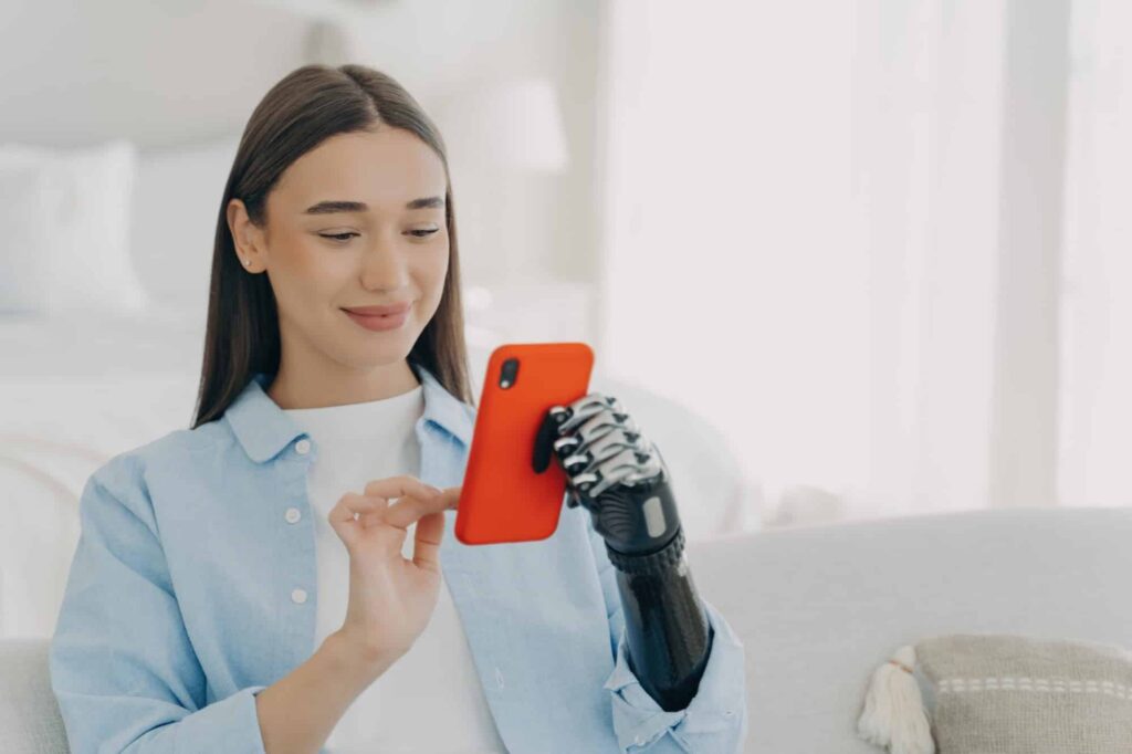 Smiling young woman with prosthetic arm using smartphone, experiencing accessibility technology at h