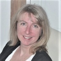 Smiling woman with blonde hair sitting indoors.